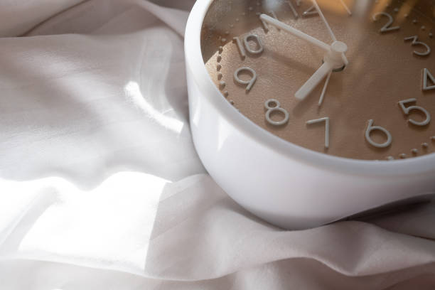 Alarm clock in bed with white blanket, top view, early rise concept, insomnia, daily routine and healthy sleep. Health concept