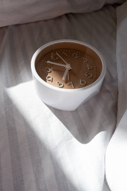 Alarm clock in bed with white blanket, top view, early rise concept, insomnia, daily routine and healthy sleep. Health concept