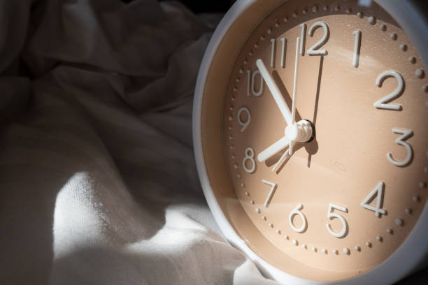 Alarm clock in bed with white blanket, top view, early rise concept, insomnia, daily routine and healthy sleep. Health concept