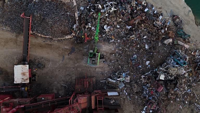 Top down static of machine grabber tossing car on pile of scrap metal in junkyard recycling center