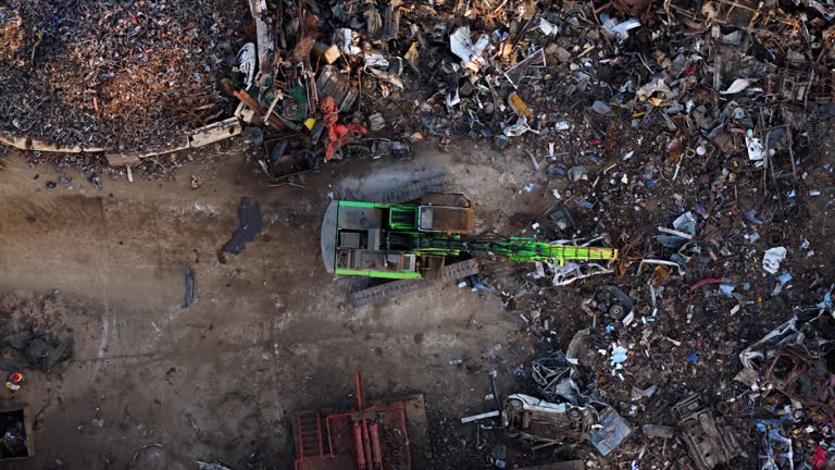 Large crane grabs broken car separating it in metal scrapyard or recycling center, aerial bird's eye view
