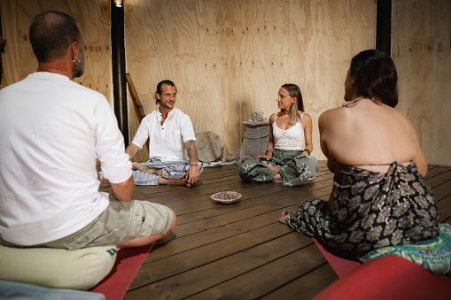 Personal therapy and self-help group hold seated conversation in lotus posture on wooden floor