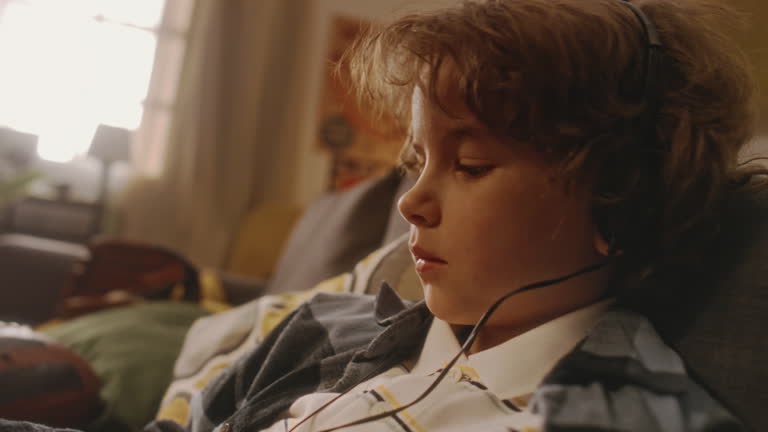 Bored Boy Choosing Good Music on Outdated MP3 Player on Sofa