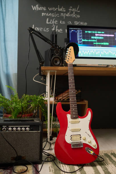 Electric guitar standing on the floor by edge of workplace of modern musician or performer with sound recording equipment