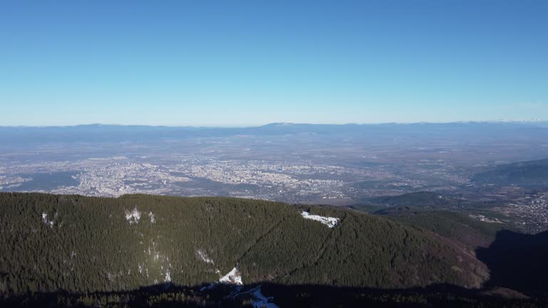 Aerial reveal clip uncovering the Sofia valley in Bulgaria and snow-covered peaks of the Stara Planina Balkan mountain range in the background on a crisp clear winter day