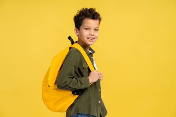 istock African American schoolboy standing in studio with yellow backpack, isolated on yellow background 2150361494
