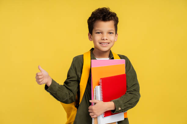 istock African American boy looking at camera, holding books, with backpack, isolated on yellow background 2150361497