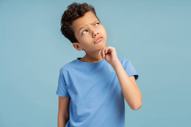 istock Boy thinking concentrated about doubt with finger on chin, in studio, isolated on blue background 2150361502