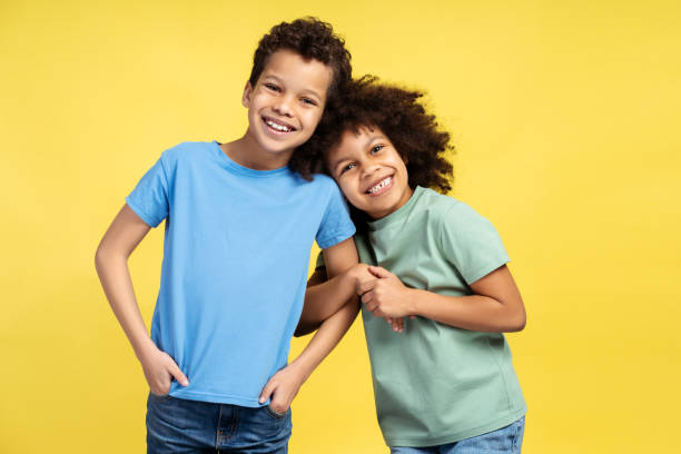 istock Happy little girl standing near boy while hugging, posing in studio, isolated on yellow background 2150361521