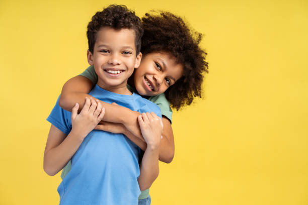 istock Smiling little girl hugging her brother while posing in studio and looking at camera 2150361525
