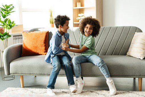 Positive, beautiful African American brother and sister fooling around together, sitting on comfortable sofa at home. Concept of childhood, family, fun