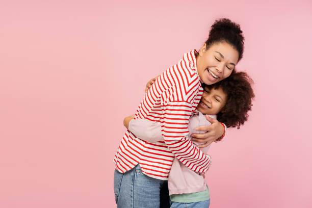 istock Happy young mother hugging her little daughter while standingin studio, isolated on pink background 2150361572