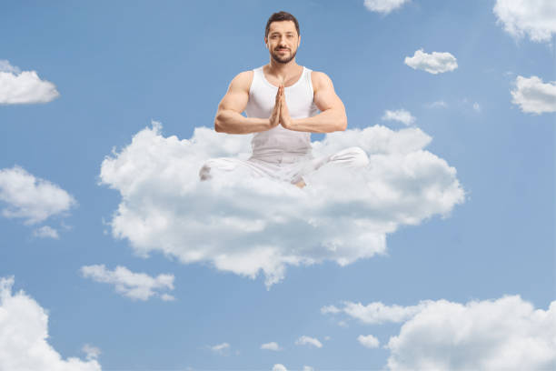 Fit young man in white clothes practicing yoga meditation up in the sky on a cloud