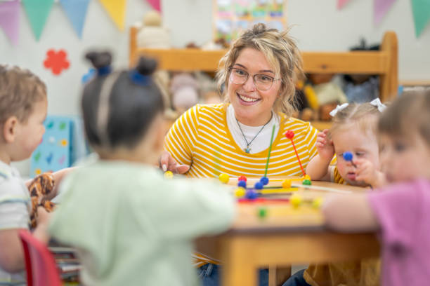 Learning Through Play A small group of preschool children sit with their teacher at a table as they learn through play. They are each dressed casually and are focused on the activity. preschool classroom jobs stock pictures, royalty-free photos & images