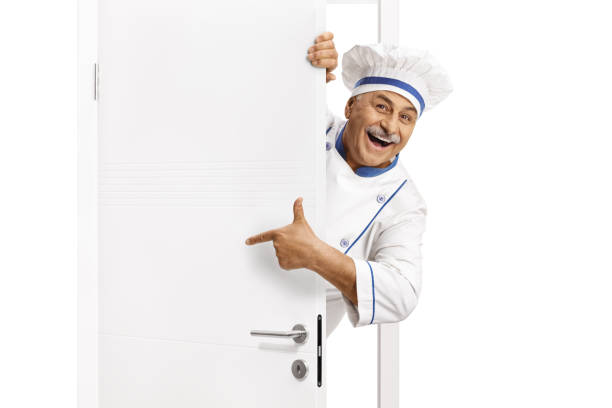 Mature chef in a uniform poitning at a door and smiling