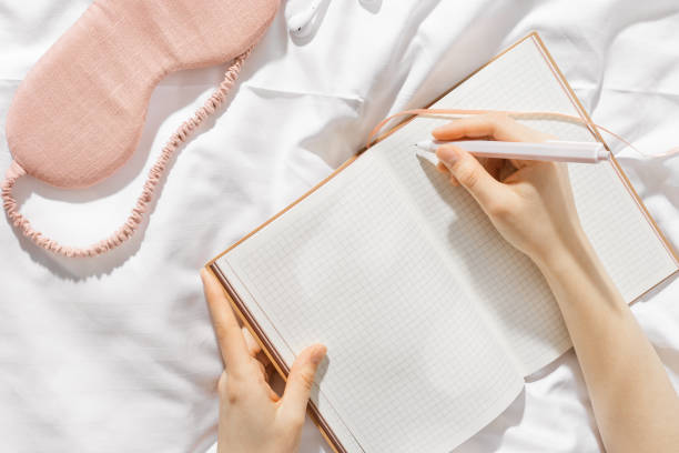 istock Woman takes notes or makes plan, day results on blank white page of paper in notebook or diary, holds notepad and pen in hands,  top view, time for yourself morning or evening before sleep 2150365414