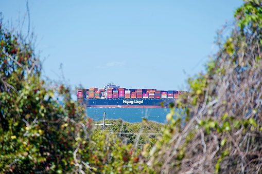 Fort Story, Virginia, USA - April 13, 2024: A Hapag-Lloyd container ship heads to sea as a Pilot Boat pulls alongside it.