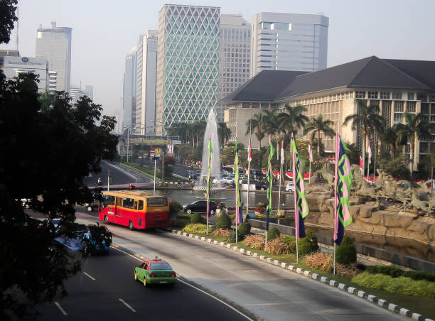 A view of Jakarta's cityscape with the fountain and Transjakarta buses and cars on the road of Merdeka Square.
