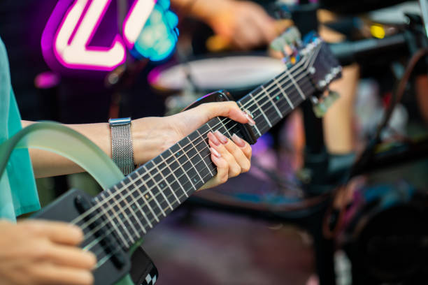 Concert view of an electric guitar player with vocalist and rock band performing in a club, male musician guitarist on stage with audience in a crowded concert hall arena, hands on a guitar
