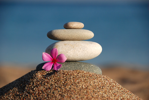 Peaceful yoga zen relaxation depiction with stacked stones and a small pink flower on sand