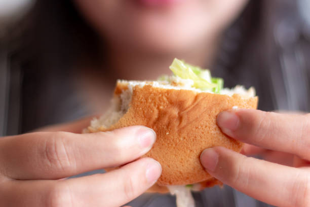 The girl is eating a sandwich with sausage.