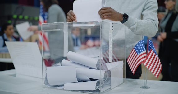 Close up shot of polling box standing on table in polling station. American voters come and put bulletins in box. Political races of US presidential candidates. National Election Day in United States.