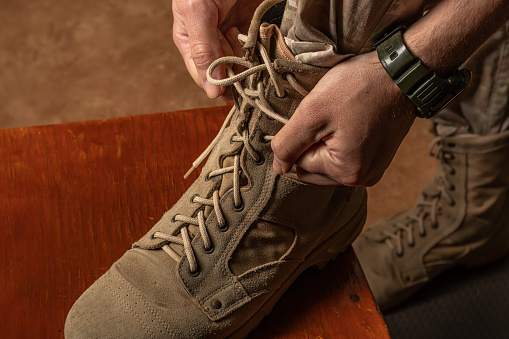 Close-up of man's hands tying laces of military boots. Beige suede army boot.