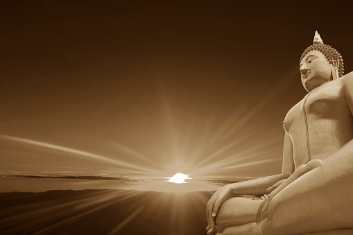 Sepia Image of Seated Buddha Image with Fantastic Sunbeams Radiating above Clouded Ocean in the Backdrop