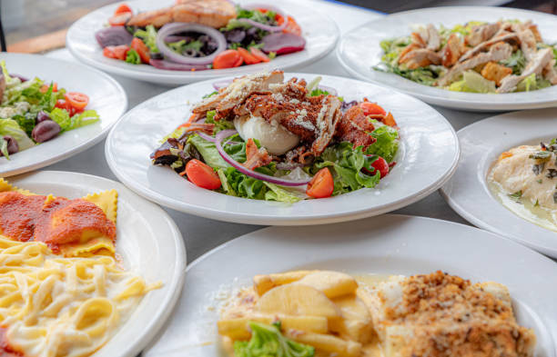 A variety of freshly prepared salads are showcased in a cafeterias food display cabinet. The salads feature vibrant greens and a mix of colorful vegetables, cheeses, and proteins, appealing to customers seeking a healthy meal option.