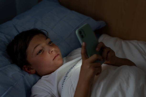 istock Boy sees cell phone lying in bed at night 2150384963
