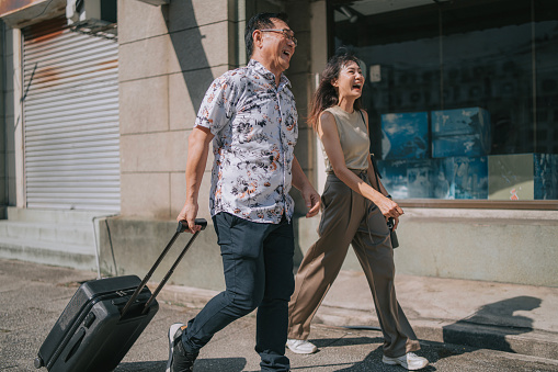 asian chinese mature couple tourist walking in Penang old town pulling carry-on luggage