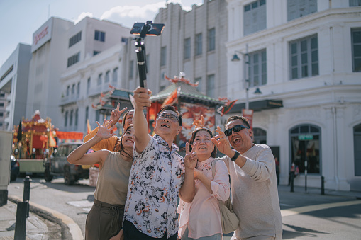 Asian mature couple tourist and malay tour guide selfie in front of parade float during chap goh meh chinese new year celebration in Penang Island