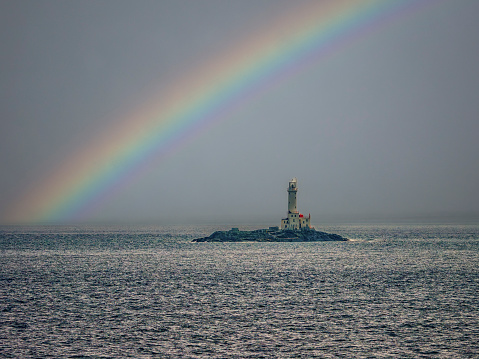 A rainbow arches over Tuskar Rock Lighthouse as it stands in the middle of the sea at location\n52°13'38.7804\
