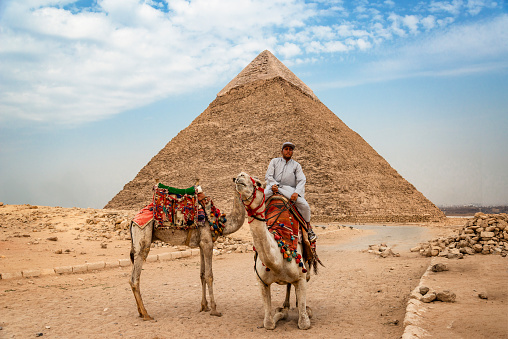 Pyramid of Khafre, Giza - October 8, 2023:  Egyptian man climbing the camel in front of the pyramid of Khafre (or the pyramid of Chephren) in Giza. Egypt, north Africa.