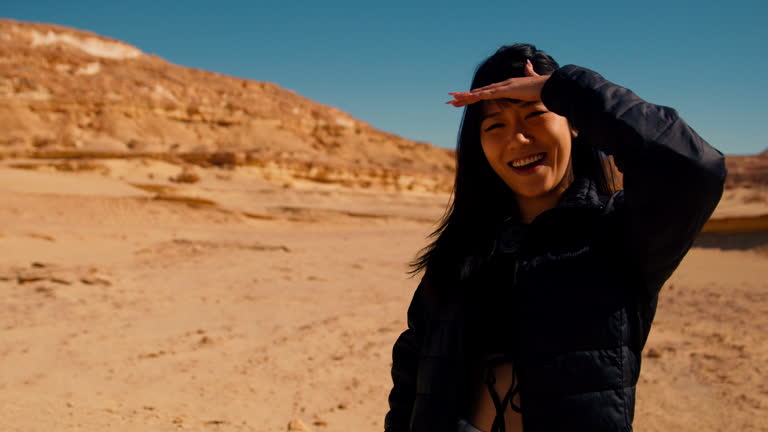 Chinese woman young girl tourist smiling in front of camera while in the desert of North Africa covering the eyes from the sunshine.
