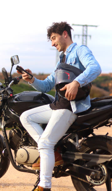 istock Curly haired Caucasian man sitting on his motorcycle using mobile 2150395500