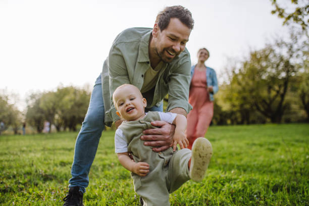 istock First steps for little toddler. Father supporting baby while walking in soft spring grass on meadow. Father's day concept. 2150396363