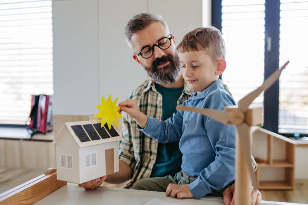 istock Father explaining renewable energy, teaching about sustainable lifestyle his young son. Playing with house with solar panels, wind turibine at home. 2150396761