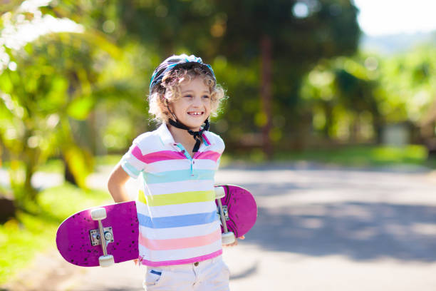 Portrait of a happy little boy is holding a skateboard in a skateboard park and looking at camera