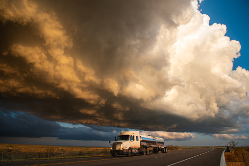 Truck passing under building storm clouds, infused with vibrant sunset hues, capturing the dynamic contrast of nature's elements in motion.