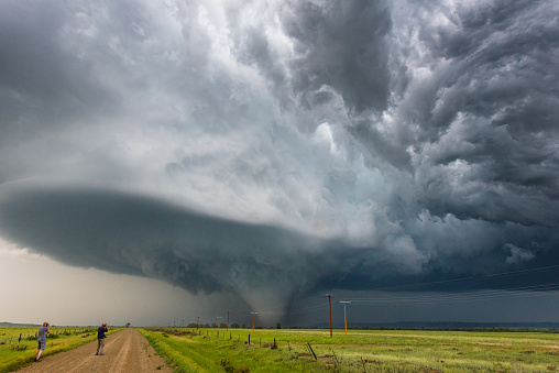 Storm chasers document a tornado beneath a dramatic supercell storm along a rural dirt road in scenic Montana.