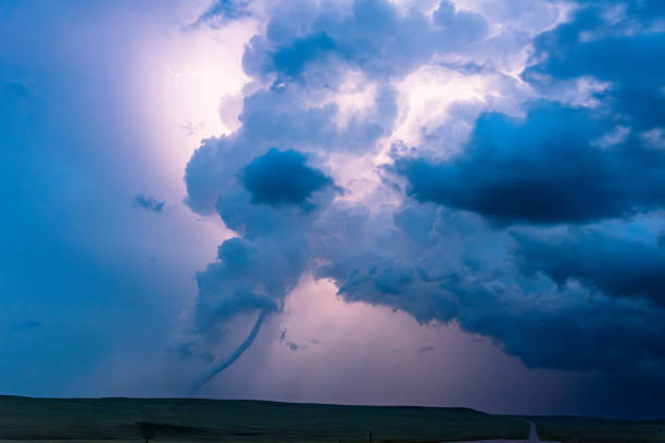 Tornado below a dark storm cloud illuminated by flashes of lightning.