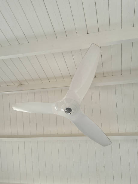 istock Image of three blade, white ceiling fan not in use, white wood ceiling and beams, low angle 2150399577