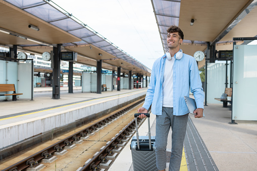 Young man holding a laptop and walking with a suitcase on a train station