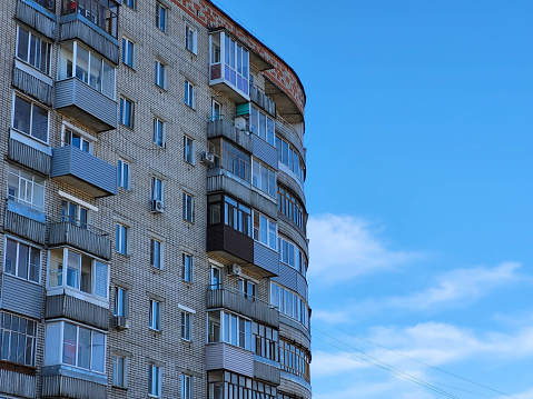 The facade of a high-rise semicircular house with balconies on a blue sky background.