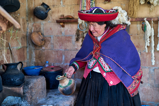 Older Quechua indigenous lady weaver in the famous town of Chinchero heating water to create colored pigments