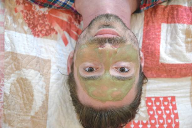 Young man with a clay face mask, skin care concept in plaid robe on white background with copy space