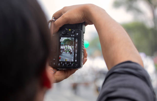 A rear view of a man taking a photo at a huge annual Day of the Dead parade that takes place in Mexico City at the end of every October. The Day of the Dead is celebrated all over Mexico at the end of October with paredes, fiestas and families observing and revering their deceased  loved ones at their graves.