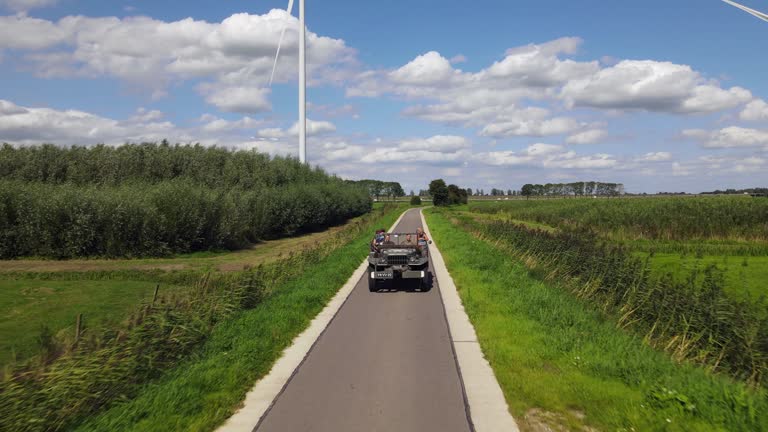Green military vehicle called Beep rides on scenic road in rural Netherlands