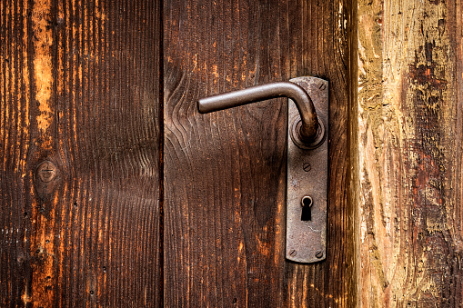 Rusty metal handle on wooden door entrance, close up